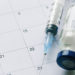 The vial with vaccine and syringe on calendar background, as a concept of vaccination season and date.