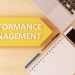 Performance Management - linear text arrow concept with notebook, smartphone, pens and coffee mug on desktop - 3d render illustration.